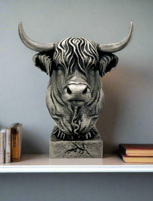 A 3D printed Highland Cow in a silver and black metallic finish. Perched on a shelf with books
