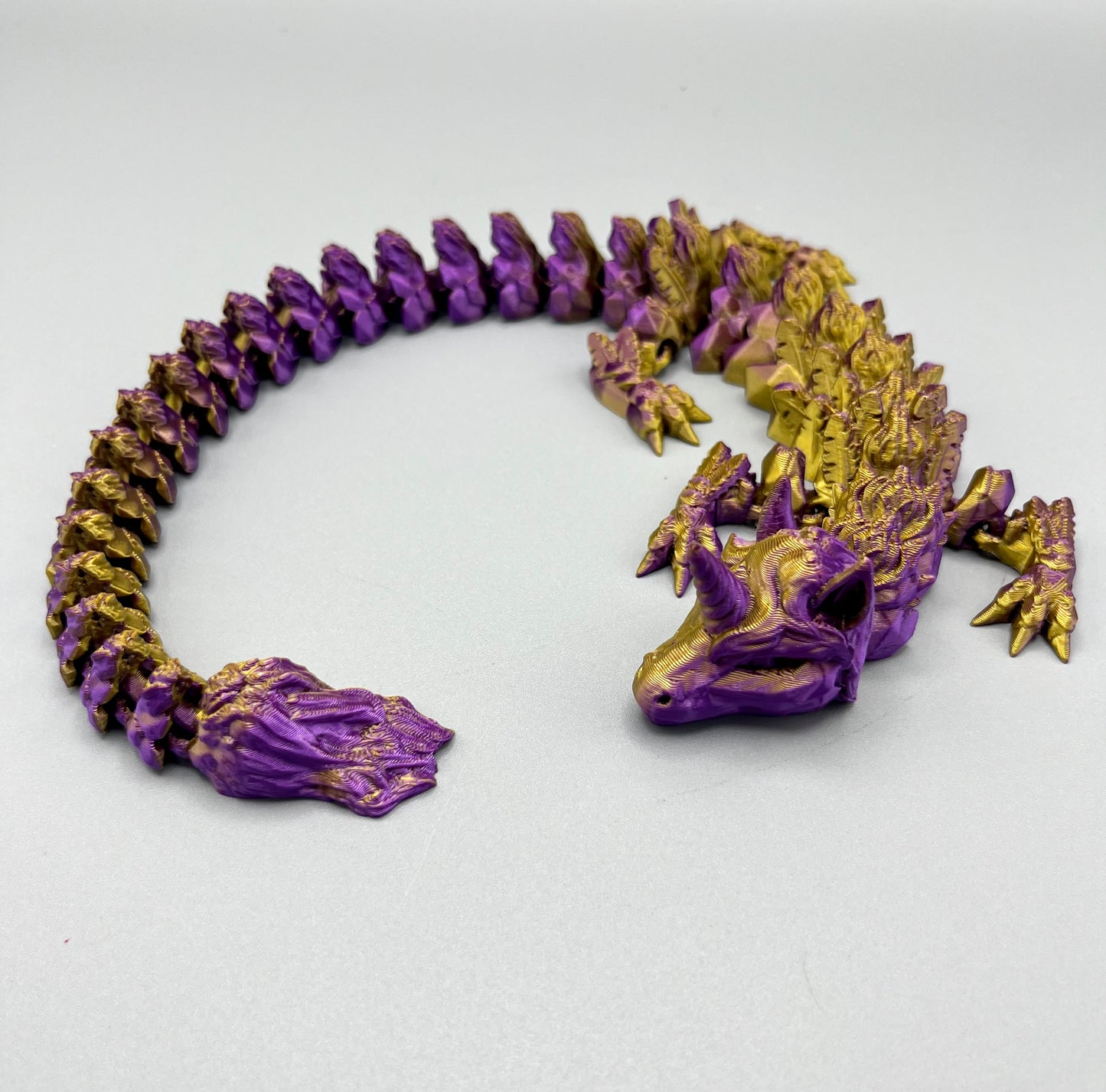 3D Printed dragon with long articulated body and the head of a unicorn, set on a light grey background
