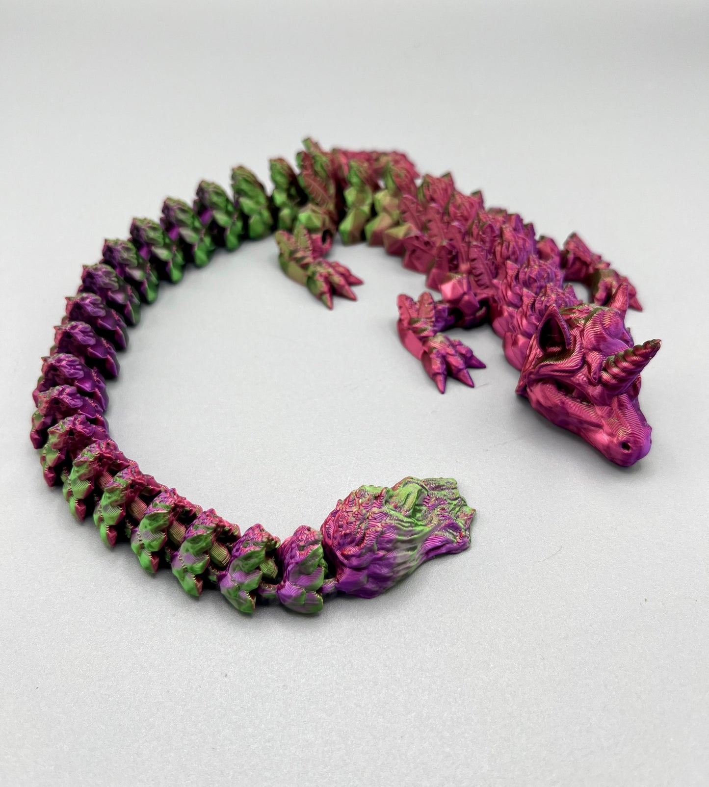 3D Printed dragon with long articulated body and the head of a unicorn, set on a light grey background