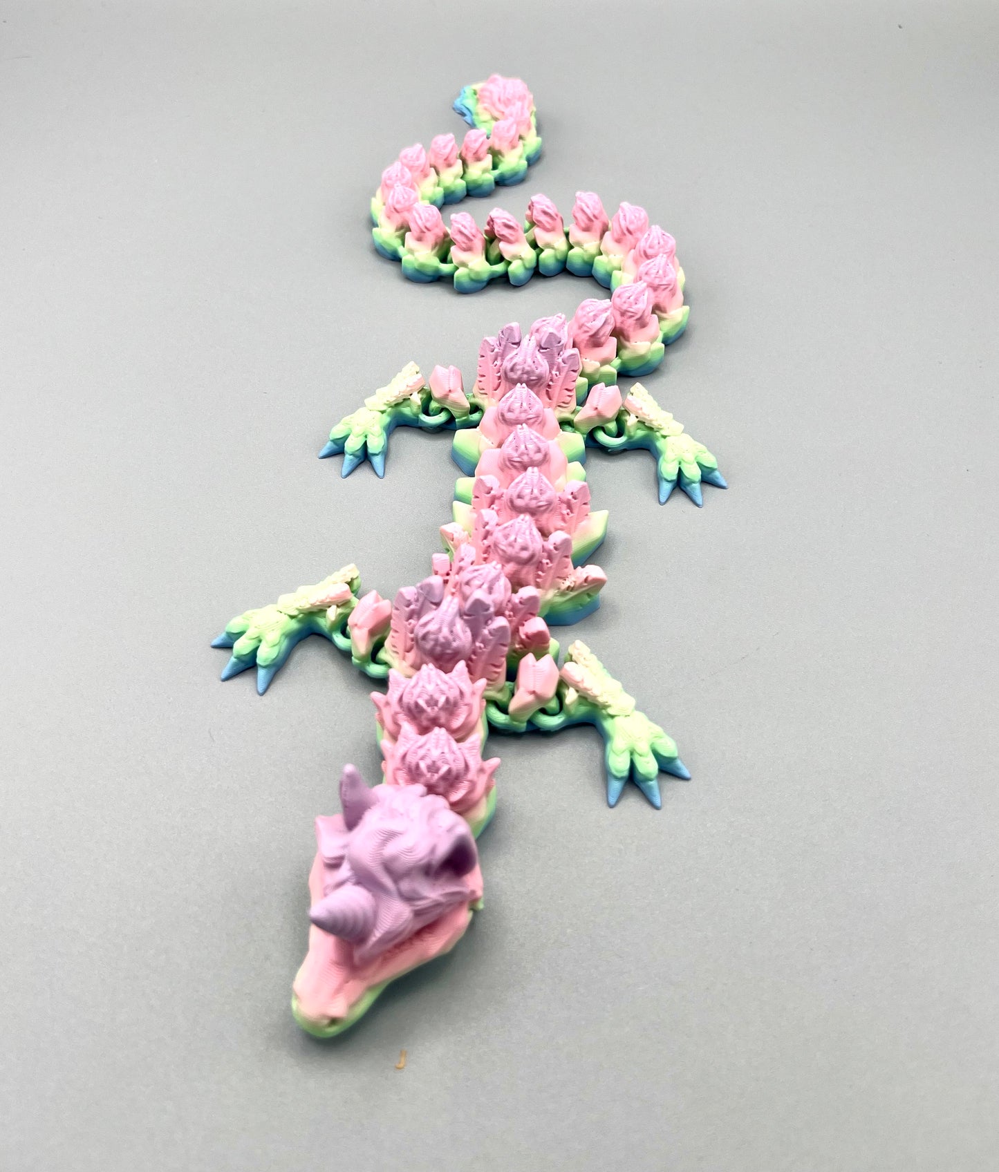 3D Printed dragon with long articulated body and the head of a unicorn, set on a light grey background