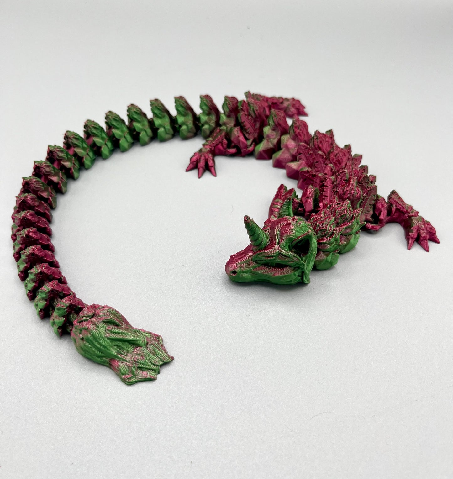 3D Printed dragon with long articulated body and the head of a unicorn, set on a light grey background