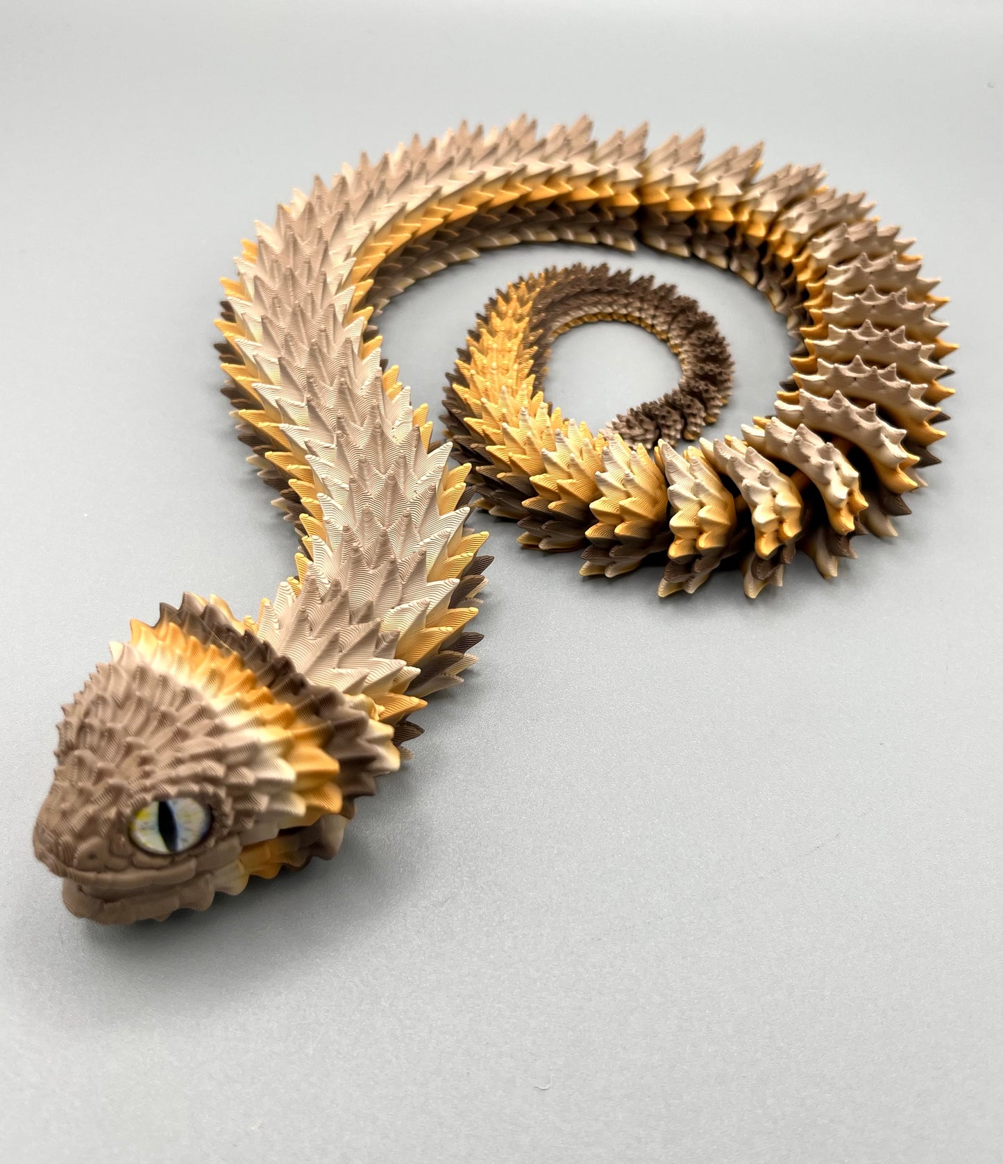 A 3D printed coffee gradient coloured Bush Viper snake, set in a coiled position, with opened mouth, realistic features and detailed scales all over. Set on a light grey background.