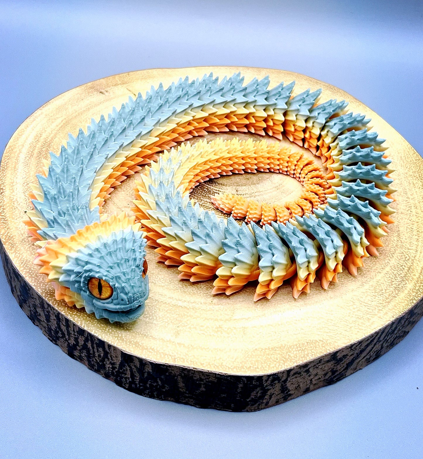 A 3D printed, khaki and orange coloured Bush Viper snake, set in a coiled position, with opened mouth, realistic features and detailed scales all over. Set on a light grey background.