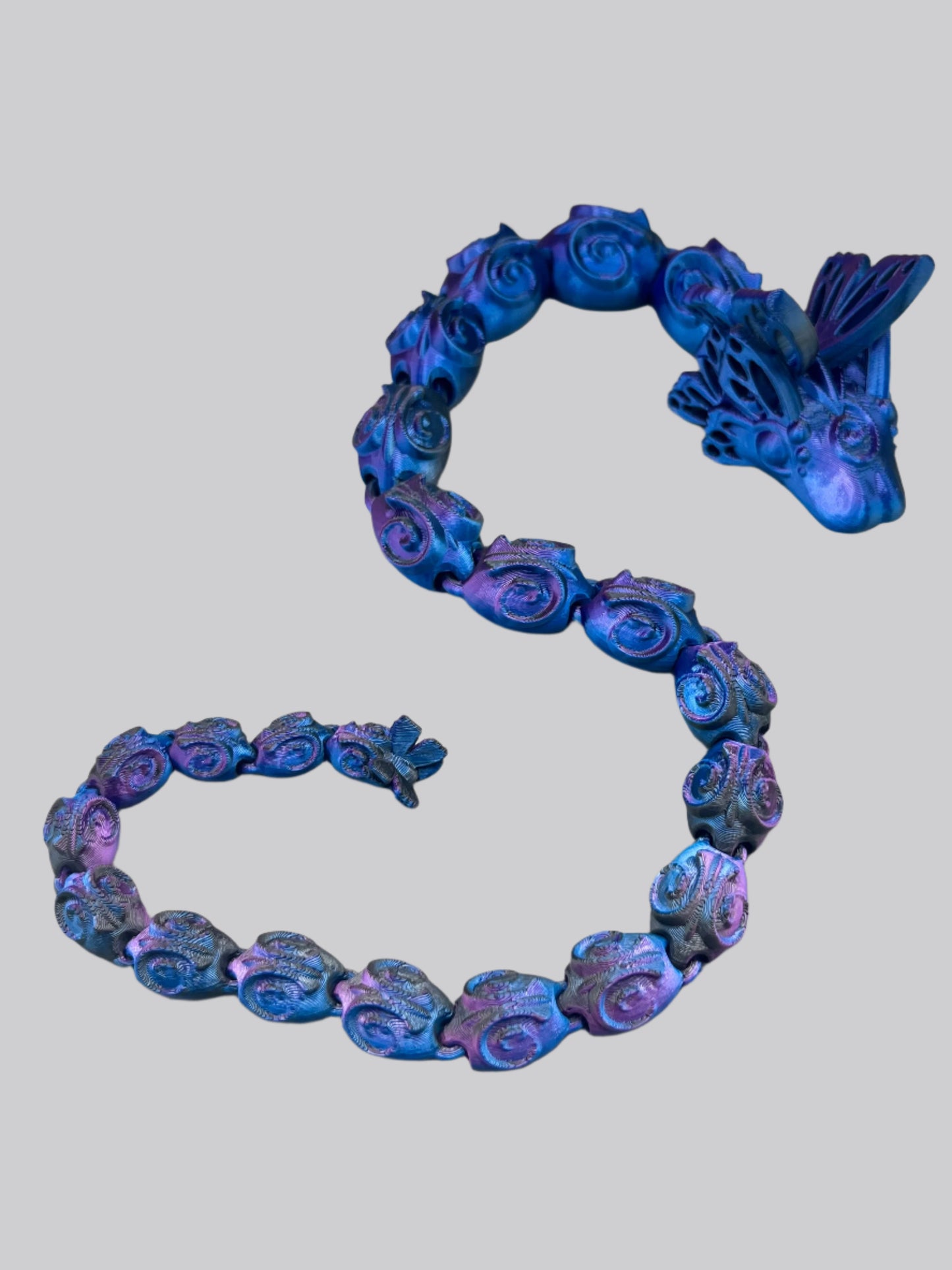 A beautiful 3D printed snake with a decoratively patterned, articulated body featuring butterfly detailing on it's head and tail.
