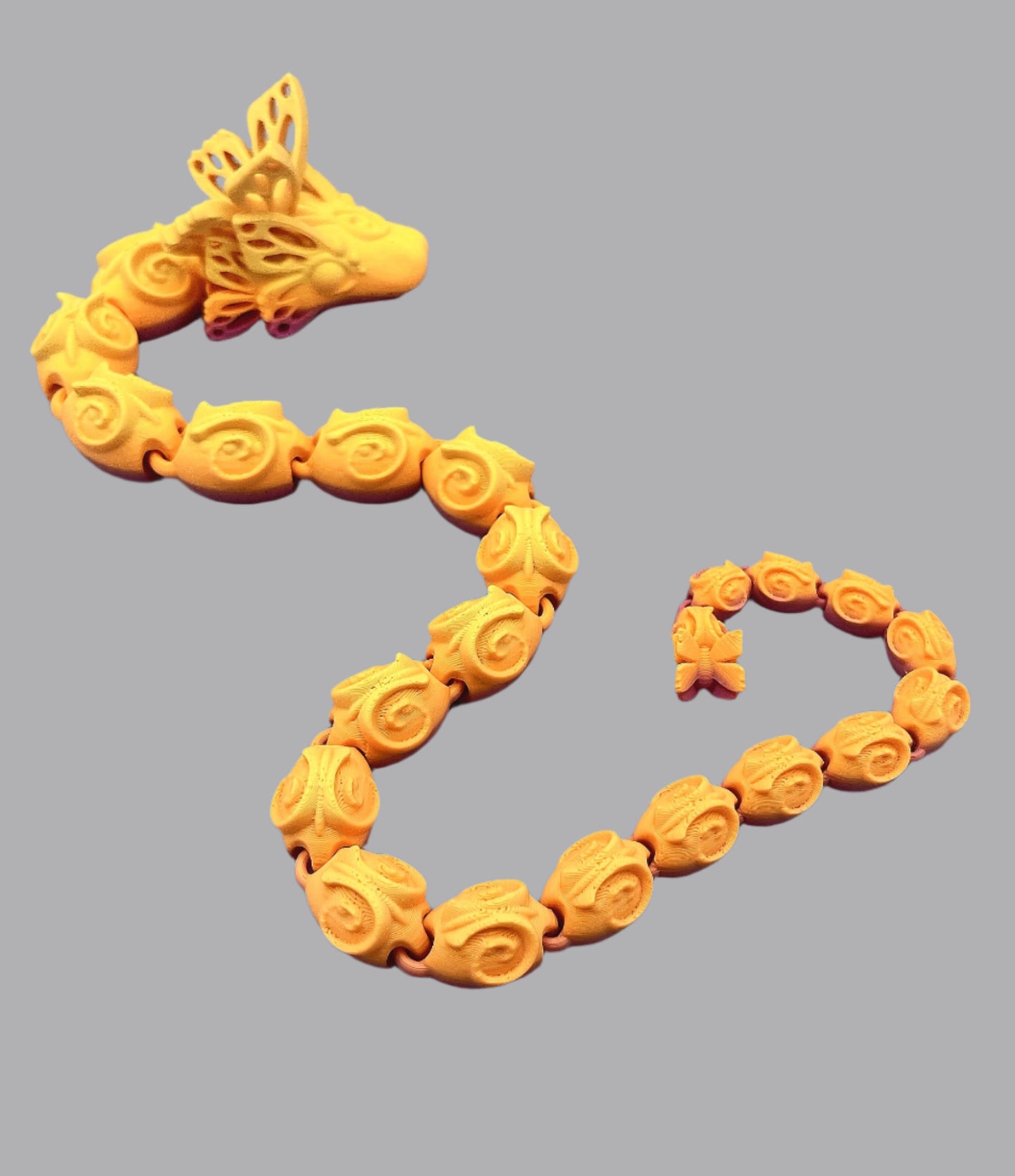 A beautiful 3D printed snake with a decoratively patterned, articulated body featuring butterfly detailing on it's head and tail. Set against a grey background.