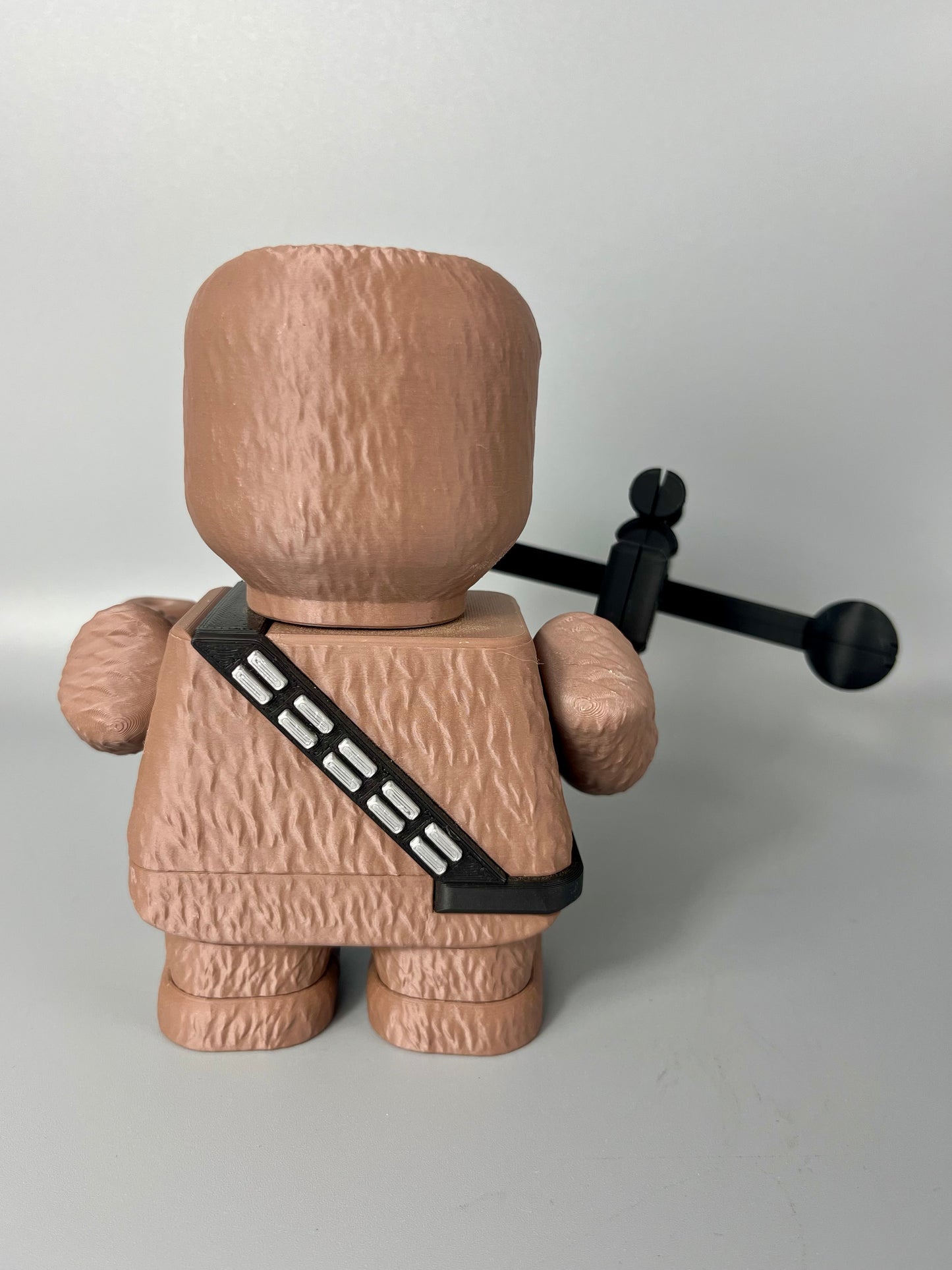 Behind view of 3D printed character with textured body and face, holding a weapon. Set on a light grey background.