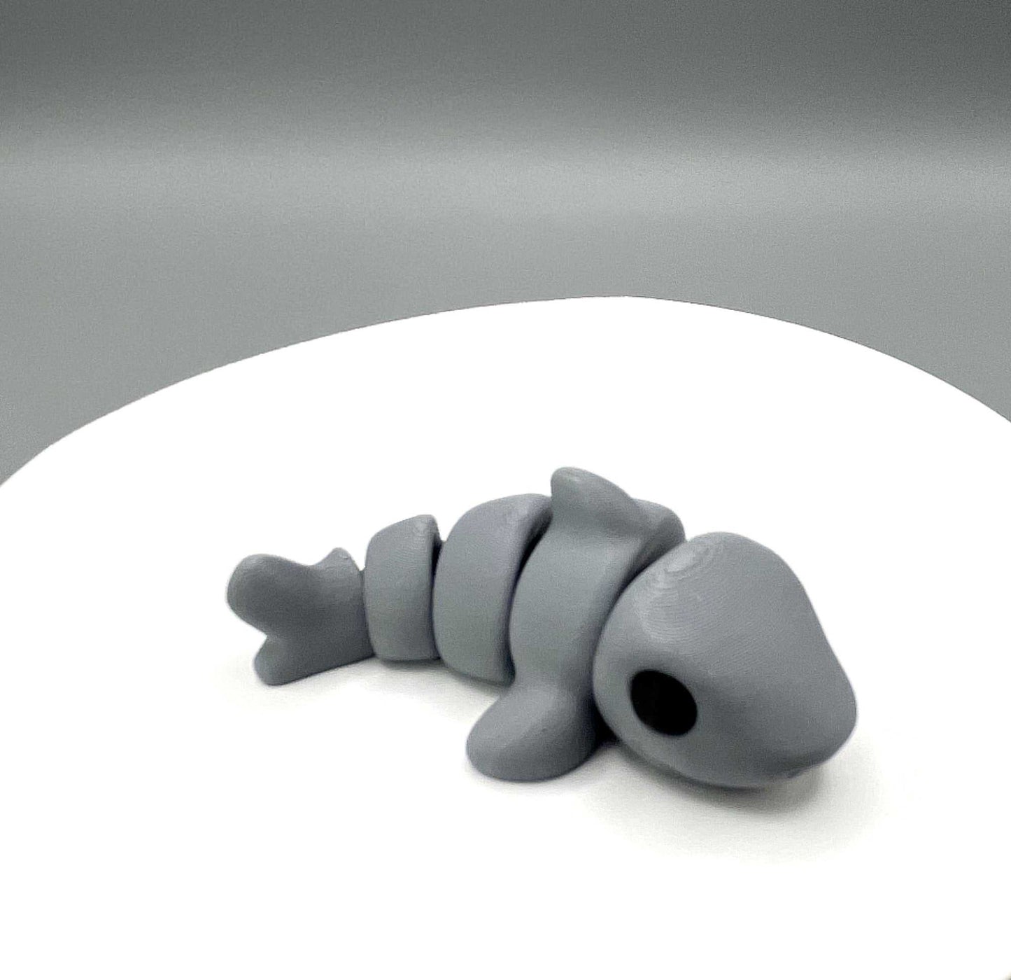 Side image of a cute eco-friendly 3D printed grey shark mini figure, with great detailing including black eyes and prominent fins. It also has articulated joints for movement.