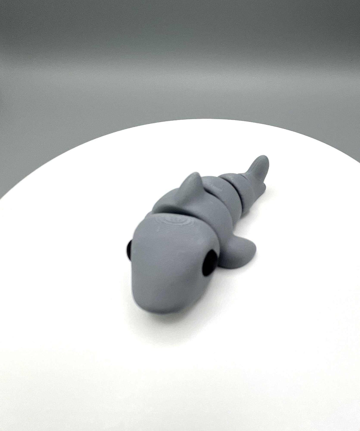 Front on image of an adorable eco-friendly 3D printed grey shark mini figure, with black eyes and prominent fins. It also has articulated joints for movement.