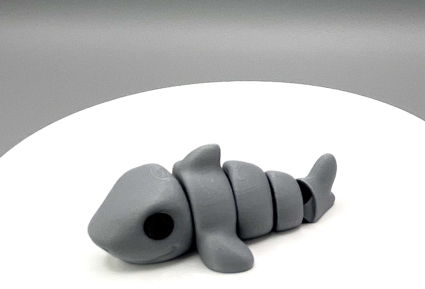 Side image of a cute eco-friendly 3D printed grey shark mini figure, capturing realistic details including black eyes and prominent fins, making this a playful choice. It also has articulated joints for movement.