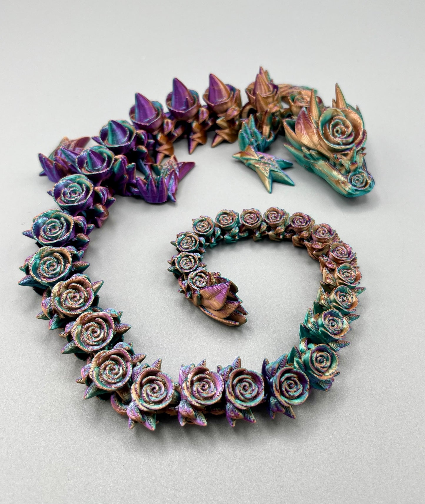 A 3D printed rose dragon, with flowers and thorns covering it's boy from head to tail.