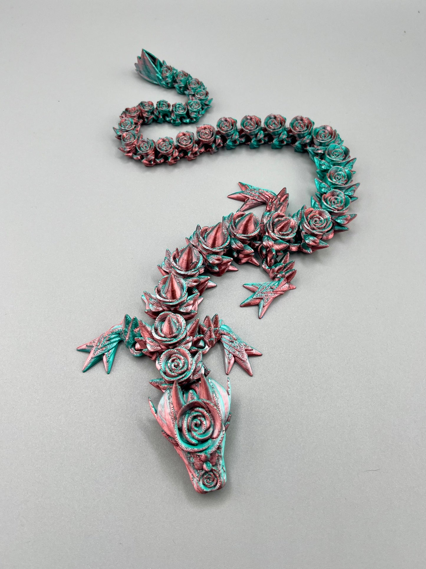 A 3D printed rose dragon, with flowers and thorns covering it's boy from head to tail.