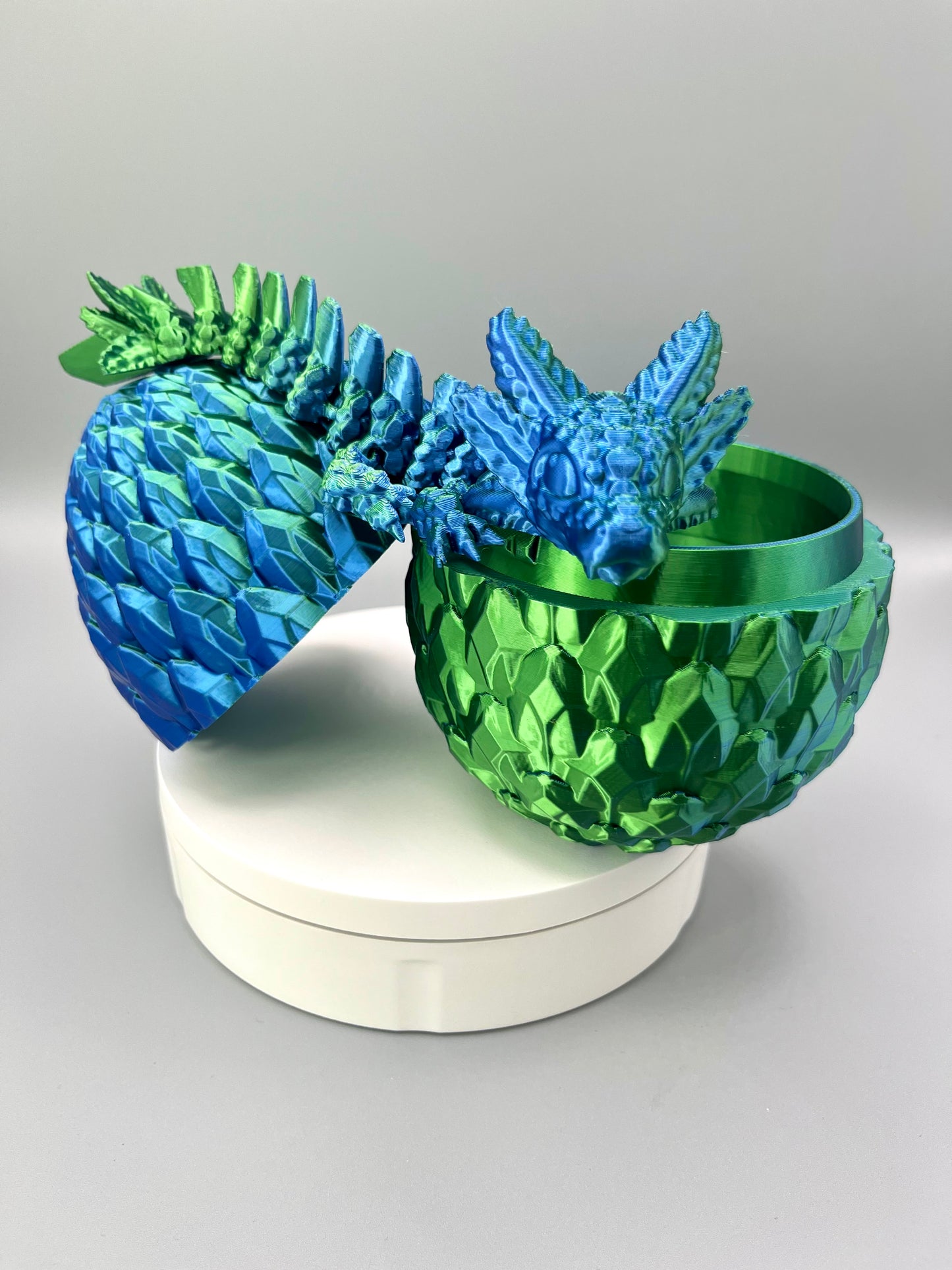 A 3D-printed set featuring a shiny axolotl dragon, sat over an open scaly egg, positioned on a white base.