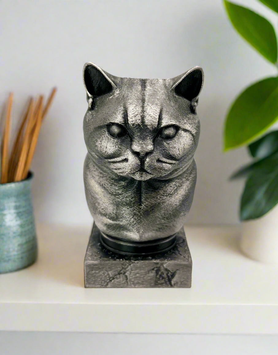A 3D printed metallic silver and black bust of a short-haired cat printed sitting on a white shelf