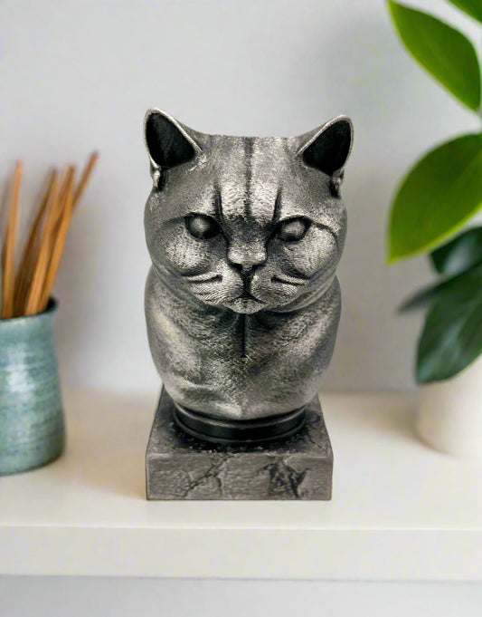 A 3D printed metallic silver and black bust of a short-haired cat printed sitting on a white shelf