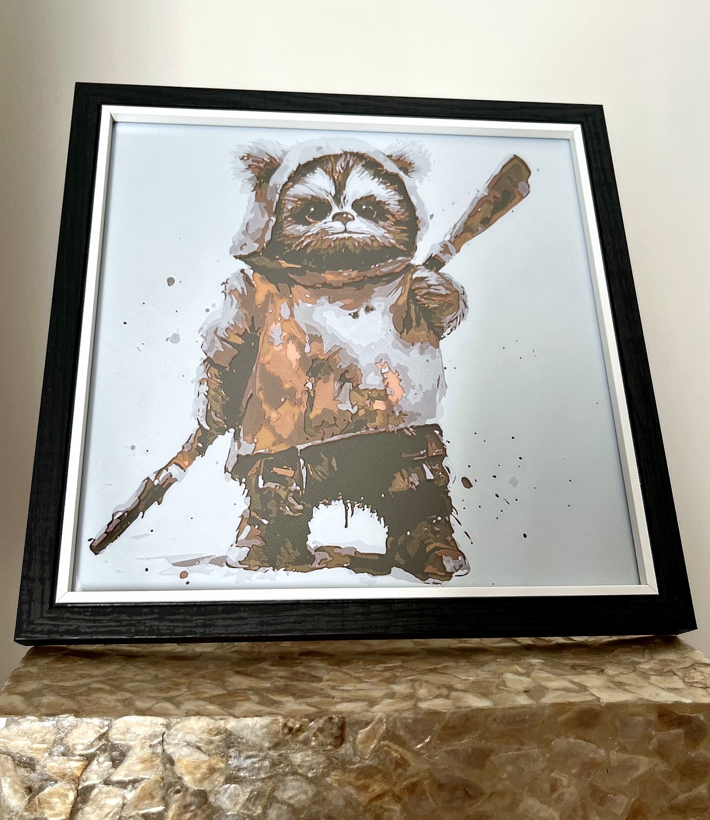 A 3D printed textured picture of an Ewok in a black frame, freestanding on a gold plinth