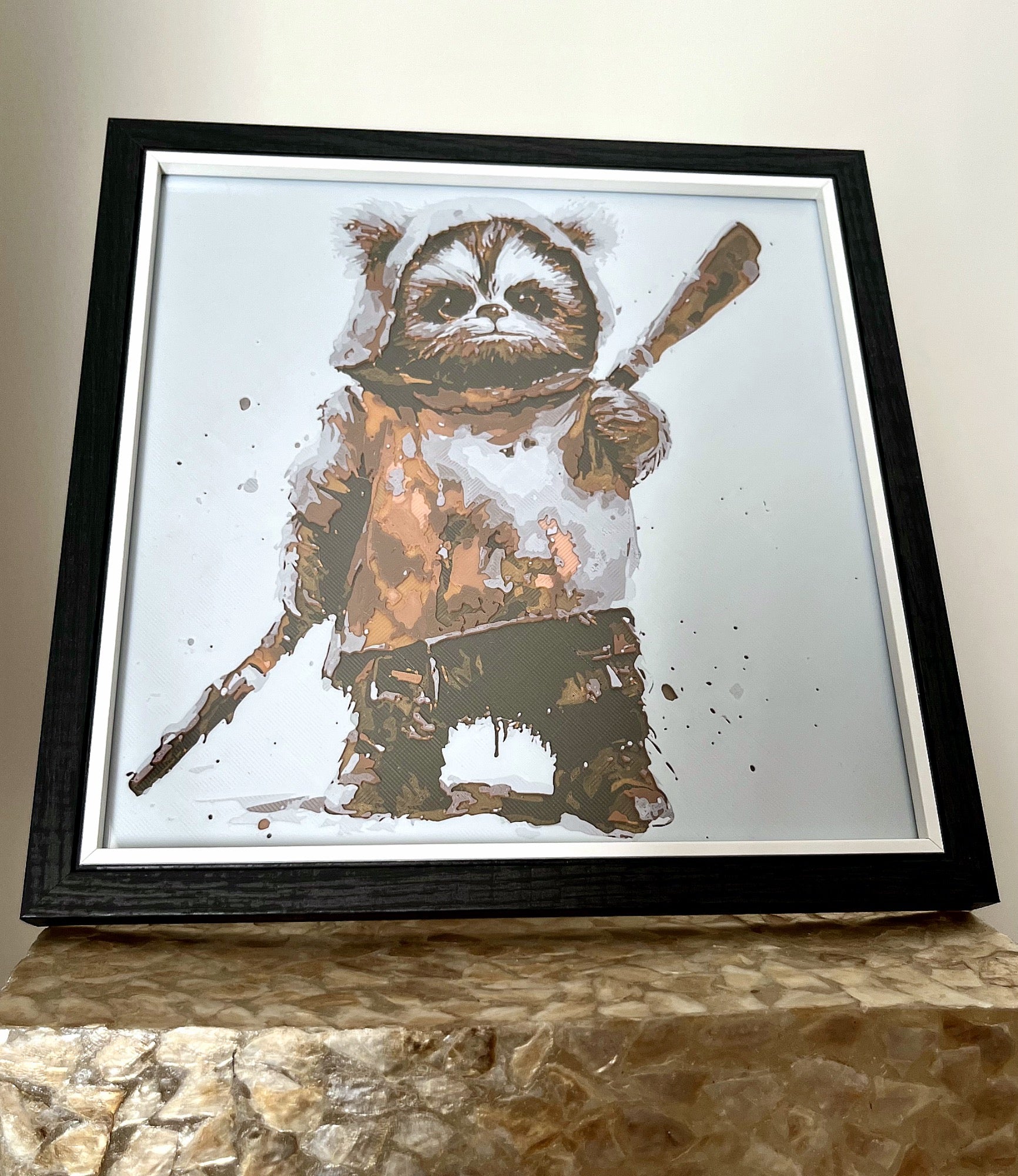 A 3D printed textured picture of an Ewok in a black frame, freestanding on a gold plinth