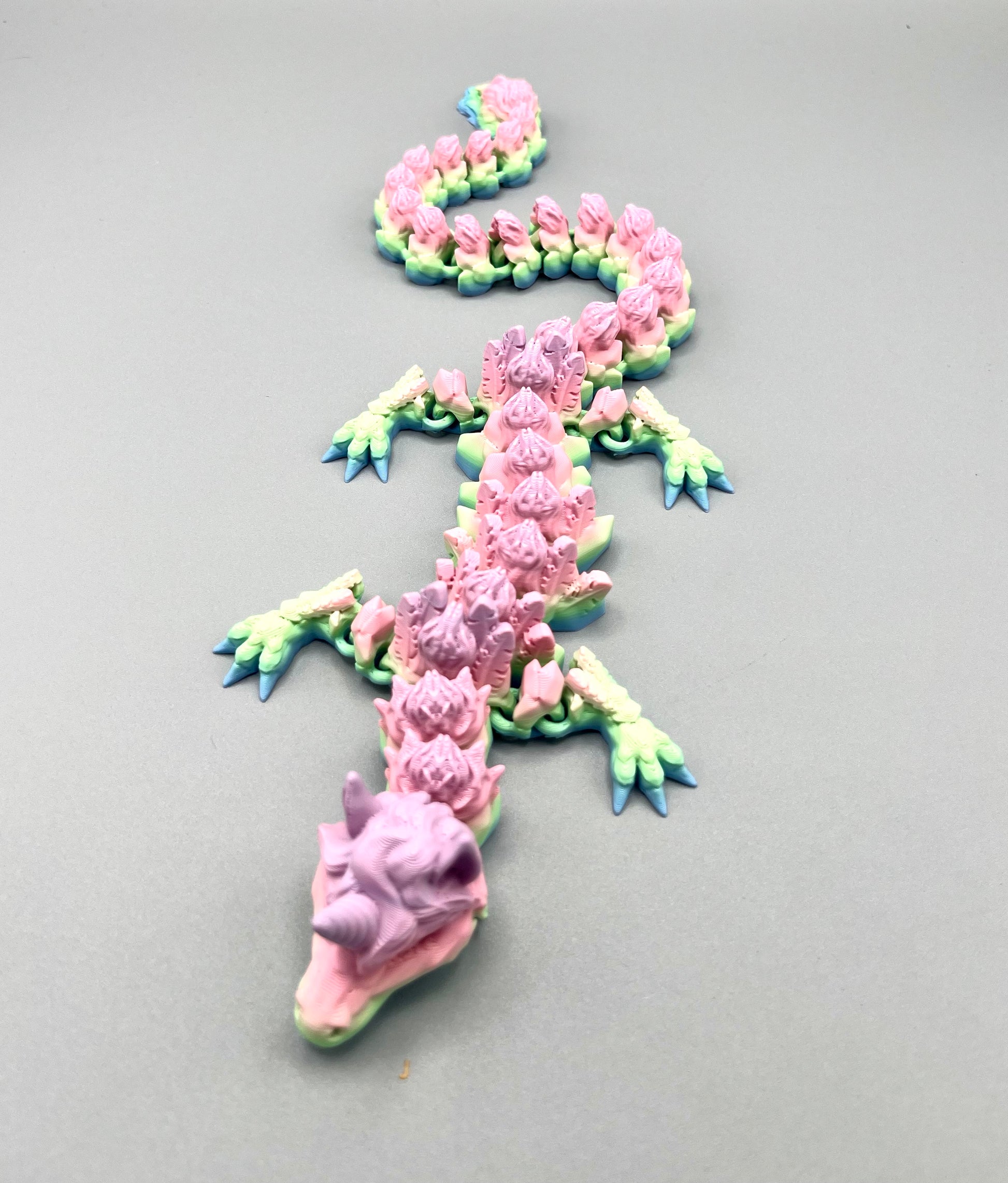 3D Printed dragon with long articulated body and the head of a unicorn, set on a light grey background