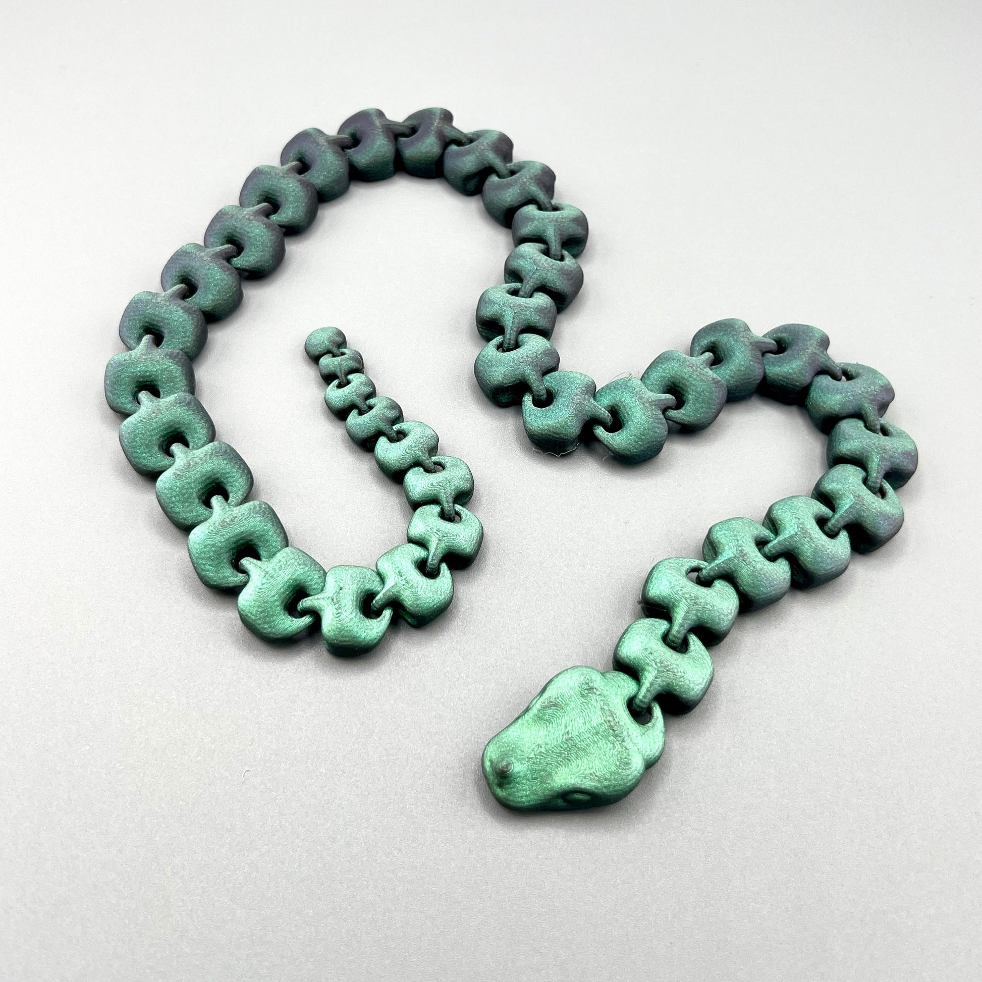 An articulated 3D-printed snake, in a shimmery finish and featuring realistic facial features.