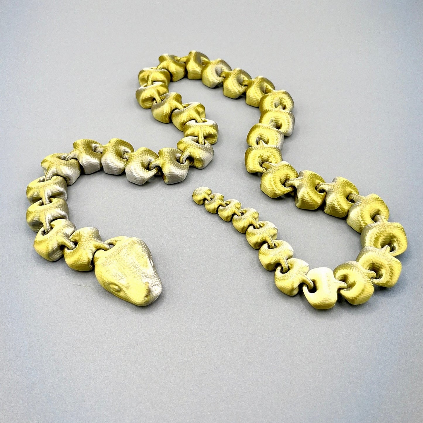 An articulated 3D-printed snake, in a shimmery finish and featuring realistic facial features.