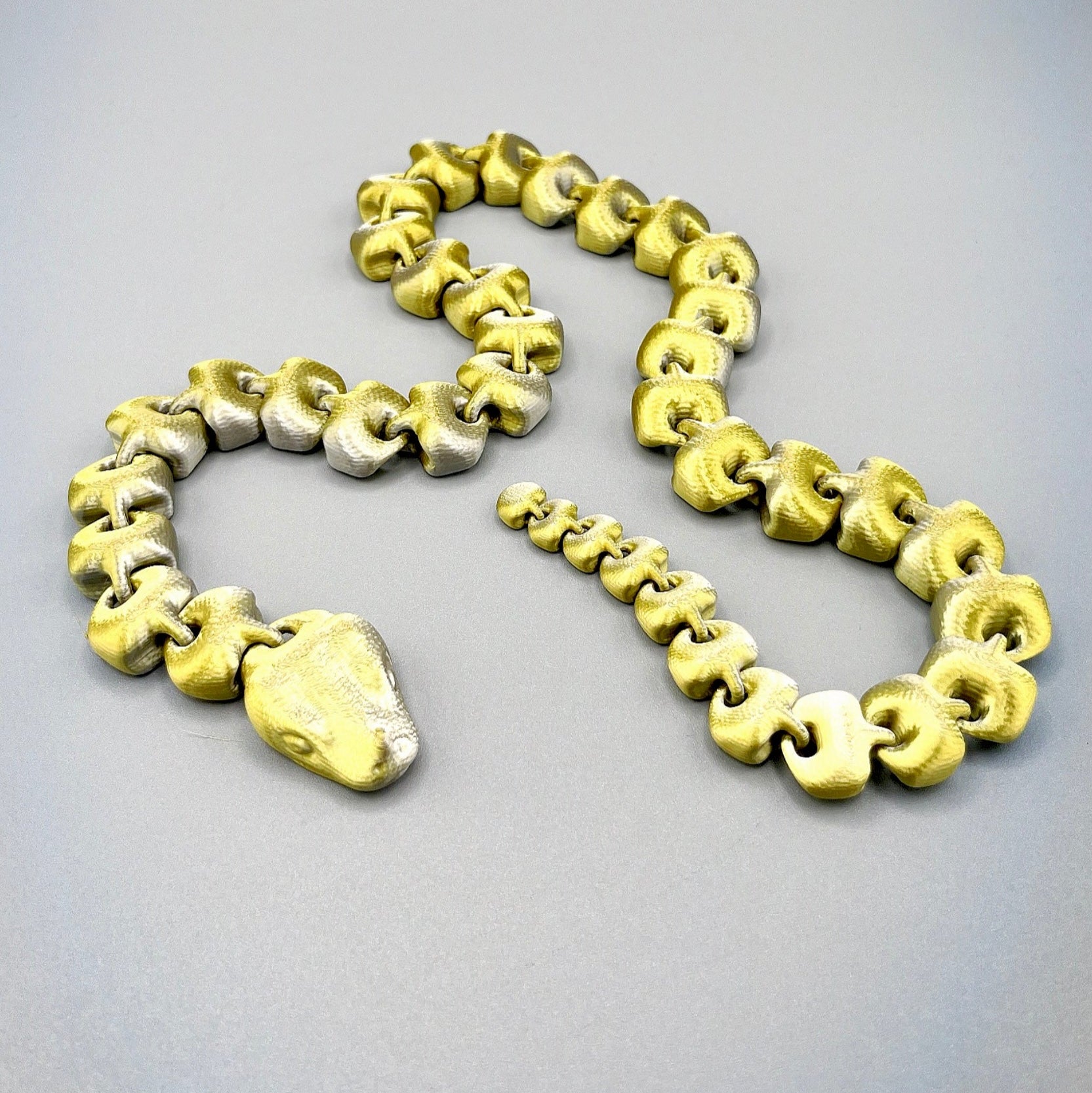 An articulated 3D-printed snake, in a shimmery finish and featuring realistic facial features.