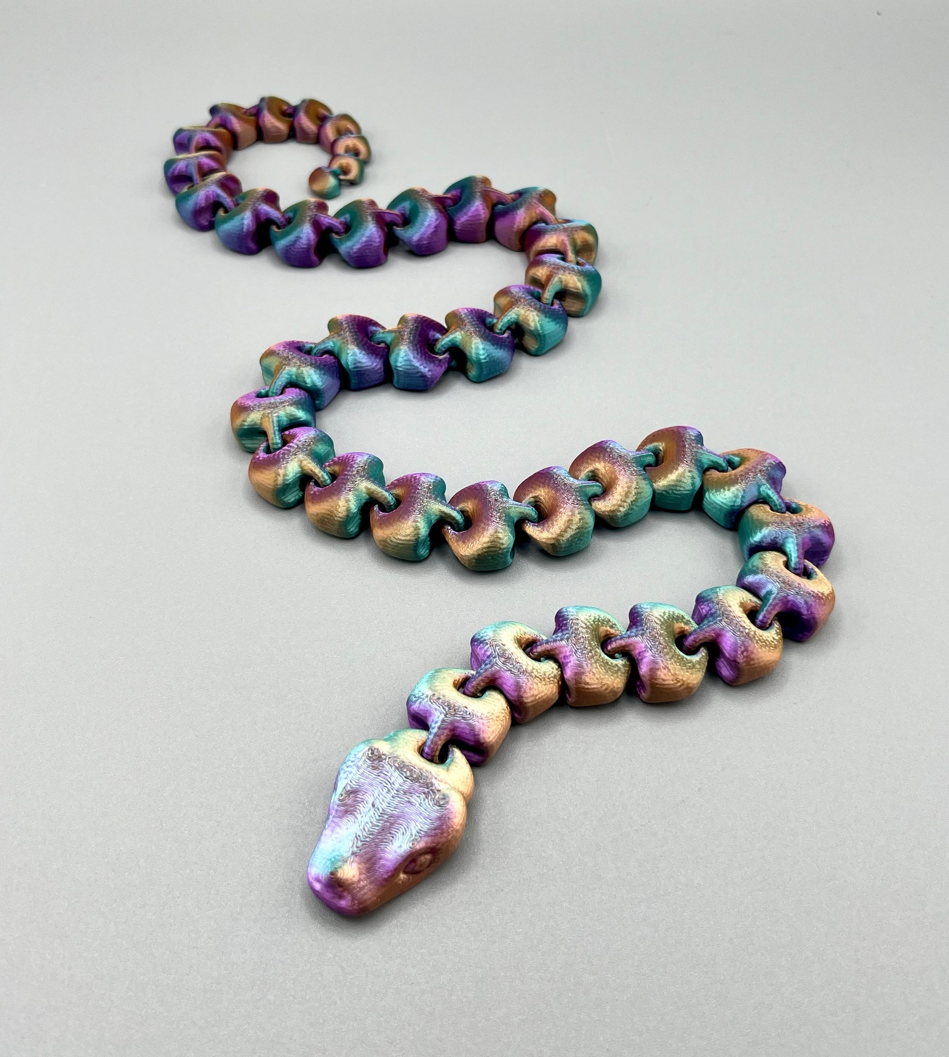 An articulated 3D-printed snake, in a shimmery finish and featuring realistic facial features.