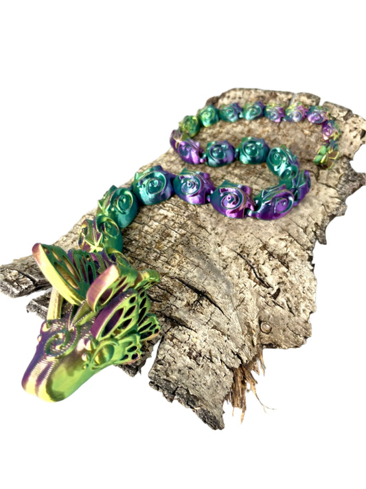 A beautiful 3D printed snake with a decoratively patterned, articulated body featuring butterfly detailing on it's head and tail. Positioned on wood and set against a light grey background.