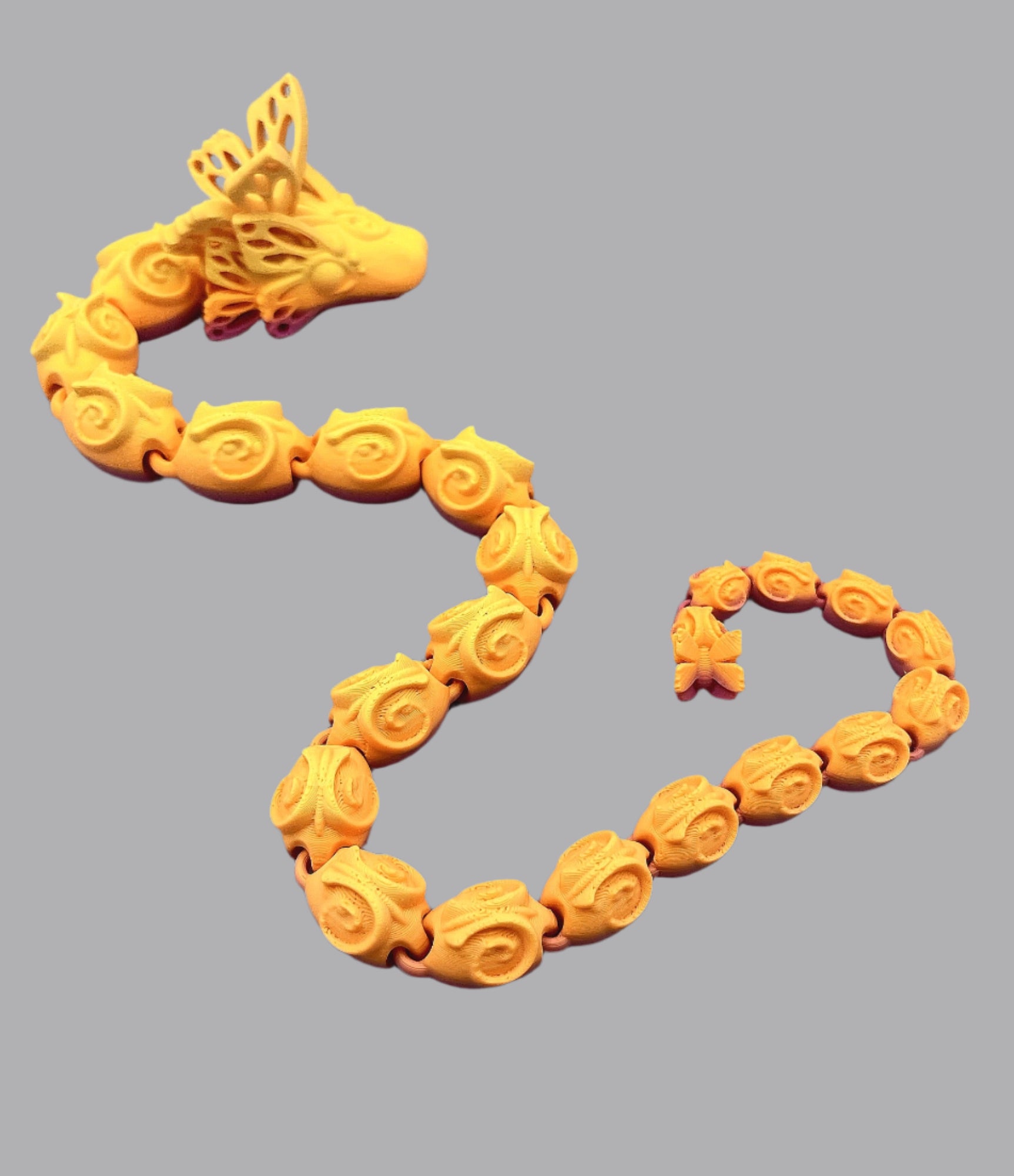 A beautiful 3D printed snake with a decoratively patterned, articulated body featuring butterfly detailing on it's head and tail. Set against a grey background.