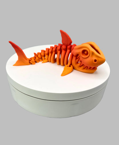A small  sized 3D printed orange gradient coloured skeleton shark figurine with detailed features and wide mouth, showing teeth. Positioned on a white display base