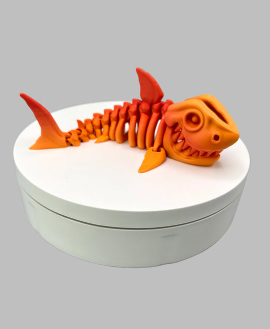 A small  sized 3D printed orange gradient coloured skeleton shark figurine with detailed features and wide mouth, showing teeth. Positioned on a white display base