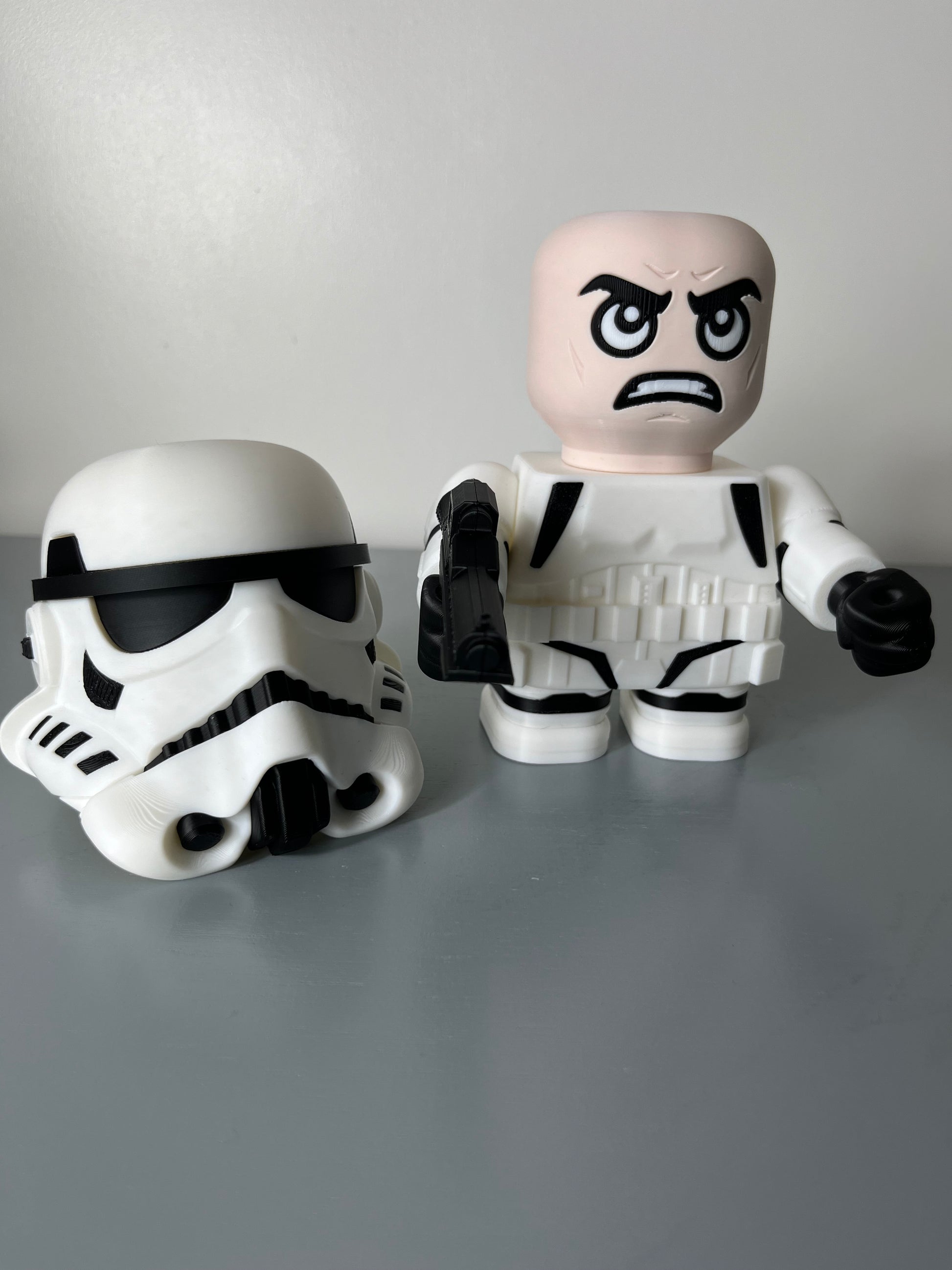 3D printed film character in a white suit with white mask removed and placed on the floor, exposing an angry looking face and holding a gun