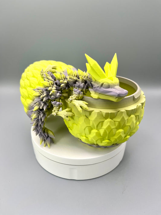 A 3D-printed dragon with intricate crystal detailing all over from head to tail, positioned laying across an open scaly egg, sat on a white base.