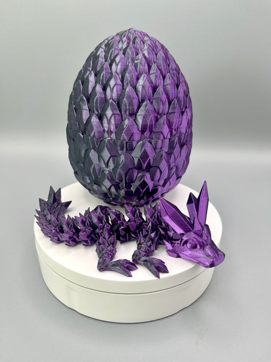 A 3D-printed dragon with intricate crystal detailing all over from head to tail, positioned laying in front of a scaly egg, sat on a white base.