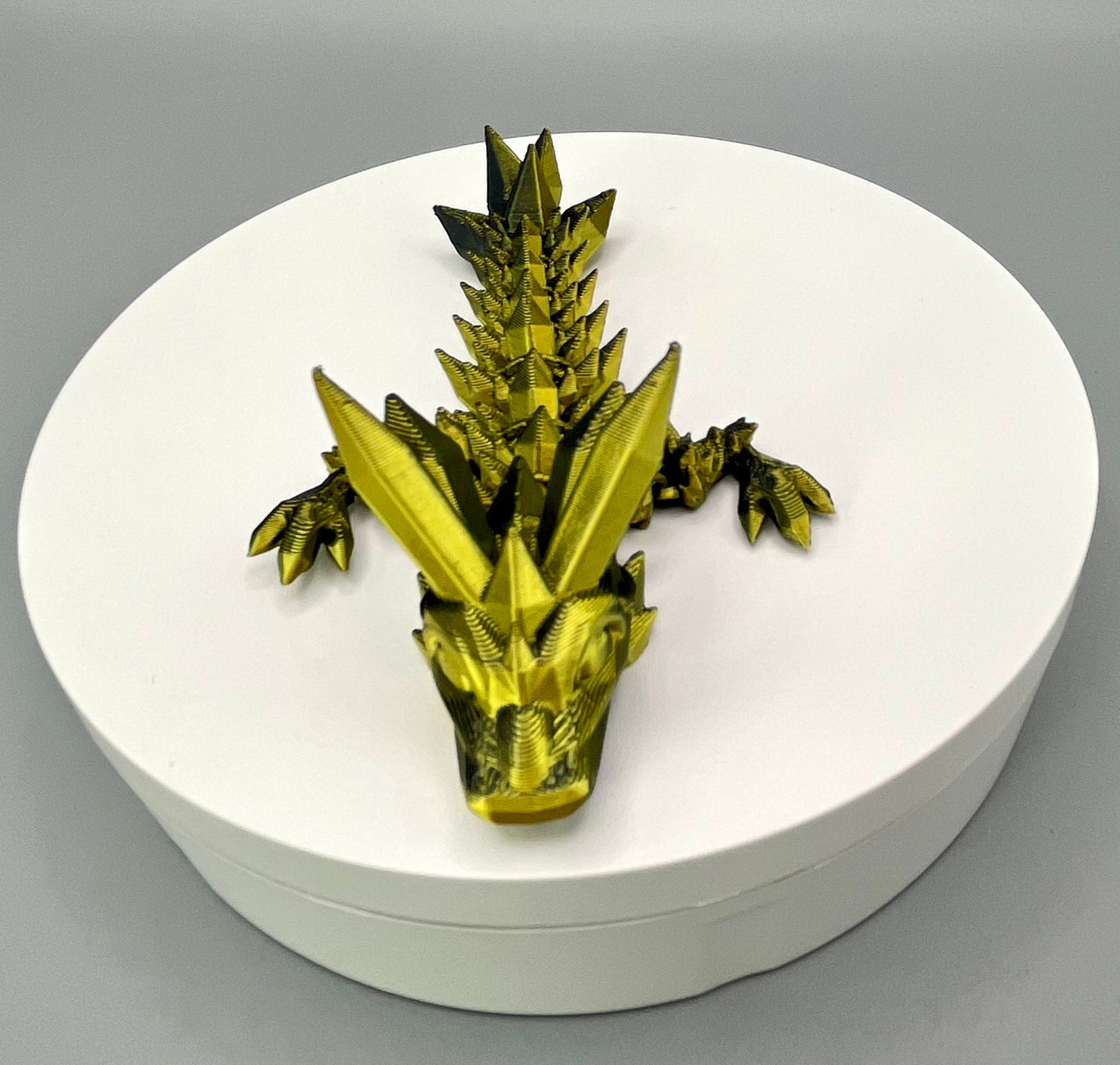 A 3D-printed small sized dragon with crystals on its head, body and tail. Positioned on a white circular base.