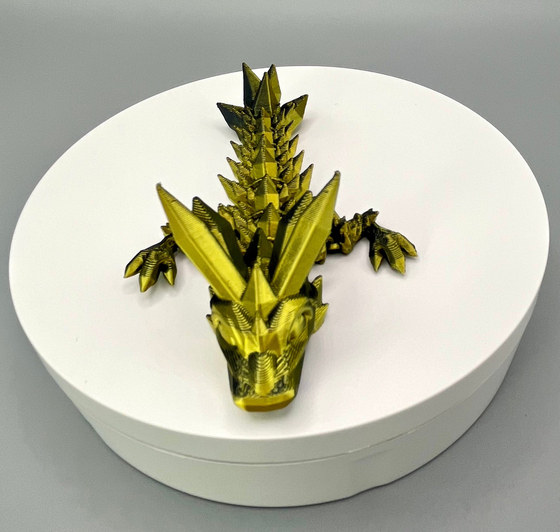 A 3D-printed small sized dragon with crystals on its head, body and tail. Positioned on a white circular base.
