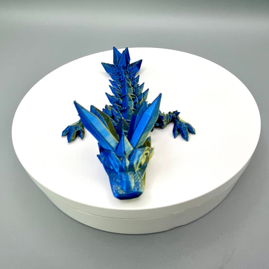 A 3D-printed small sized dragon with crystals on its head, body and tail. Positioned on a white circular base.