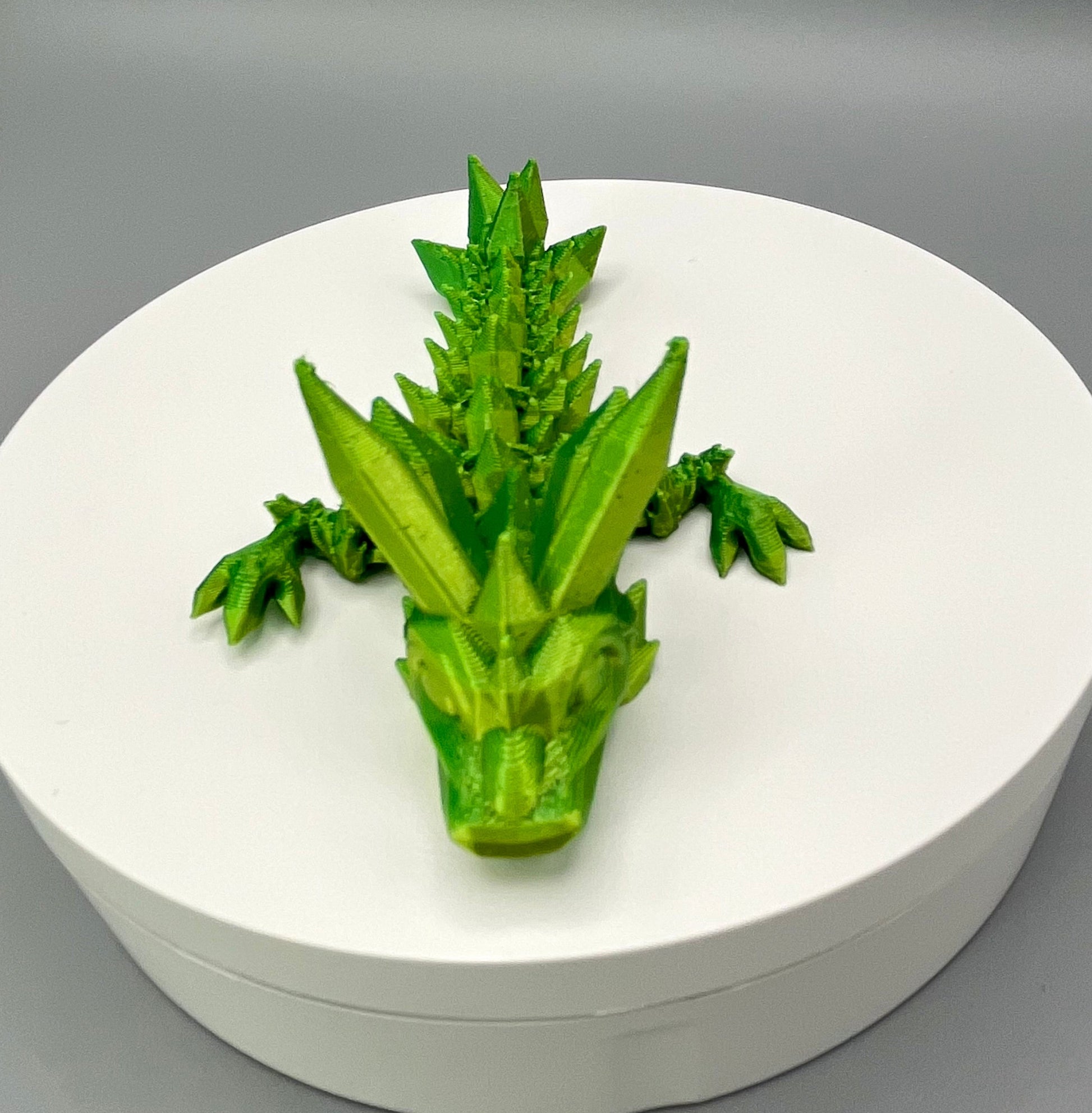 A 3D-printed small sized dragon with crystals on its head, body and tail. Positioned on a white circular base.