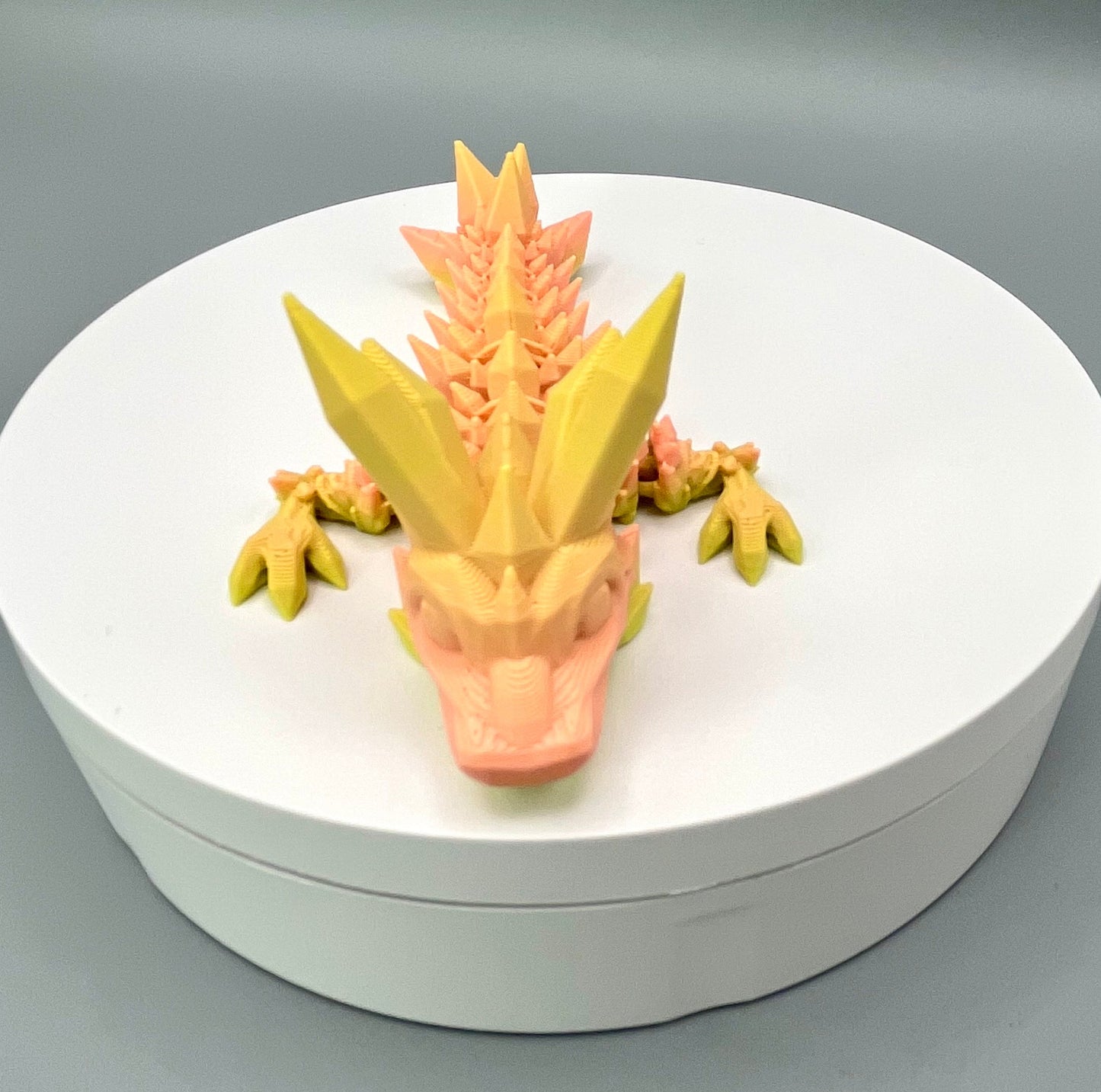 A 3D-printed small sized dragon with crystals on its head, body and tail. Positioned on a white circular base.