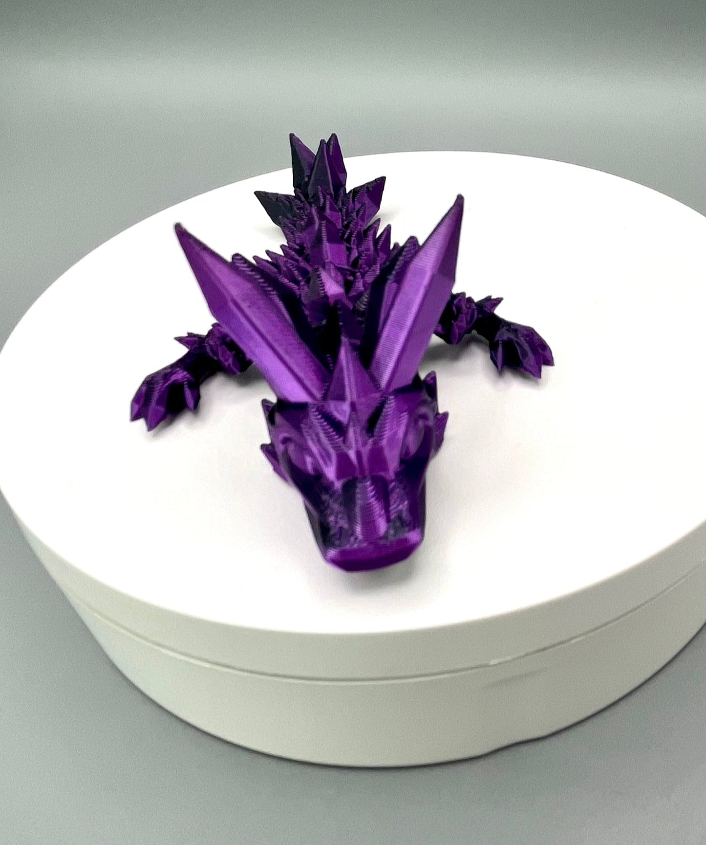 A 3D-printed small sized dragon with crystals on its head, body and tail. Positioned on a white circular base.
