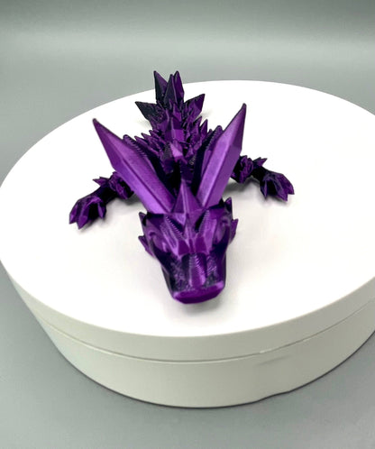 A 3D-printed small sized dragon with crystals on its head, body and tail. Positioned on a white circular base.