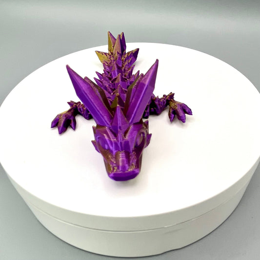 A 3D-printed small sized dragon with crystals on its head, body and tail. Positioned on a white circular base.
