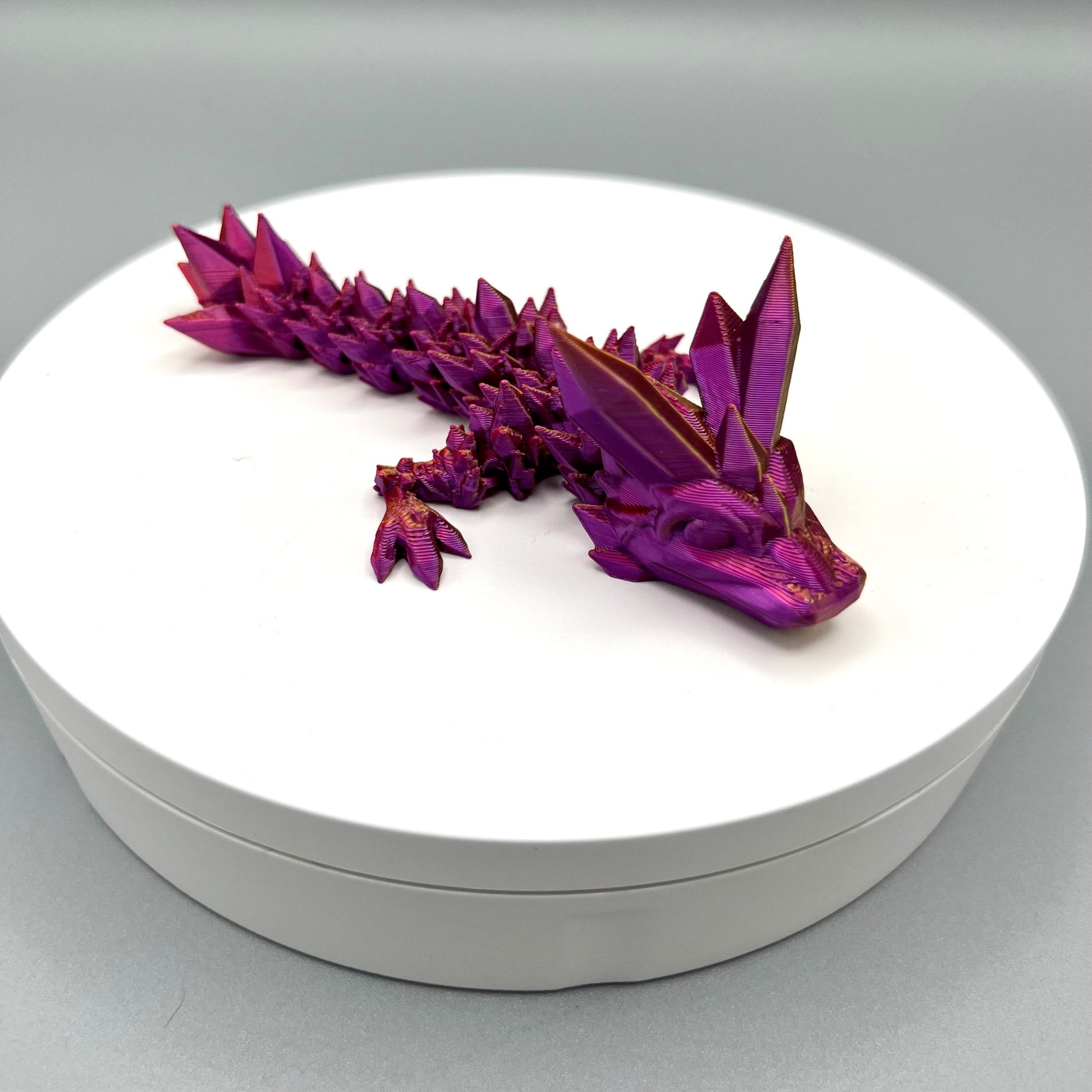 A 3D-printed small sized dragon with crystals on its head, body and tail. Positioned on a white circular base.