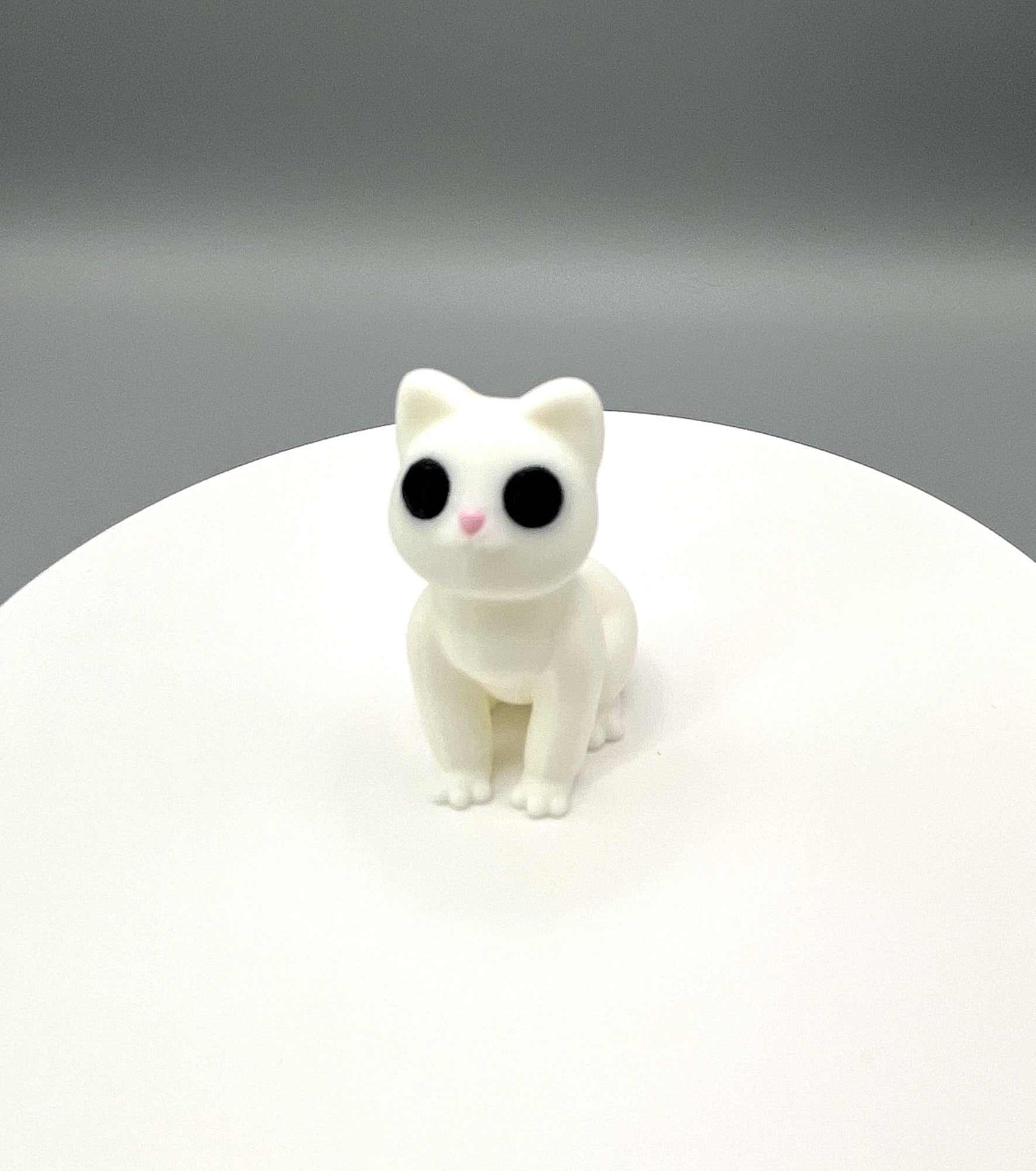 A cute 3D printed cat mini figure with pointy ears and big eyes, in a sitting position
