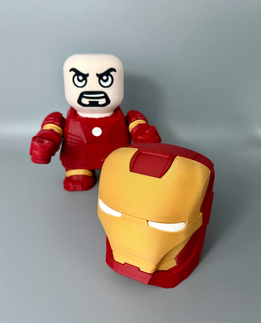 3D printed superhero with mask removed and on the floor, exposed face with goatee and red and gold superhero suit, set on a grey background