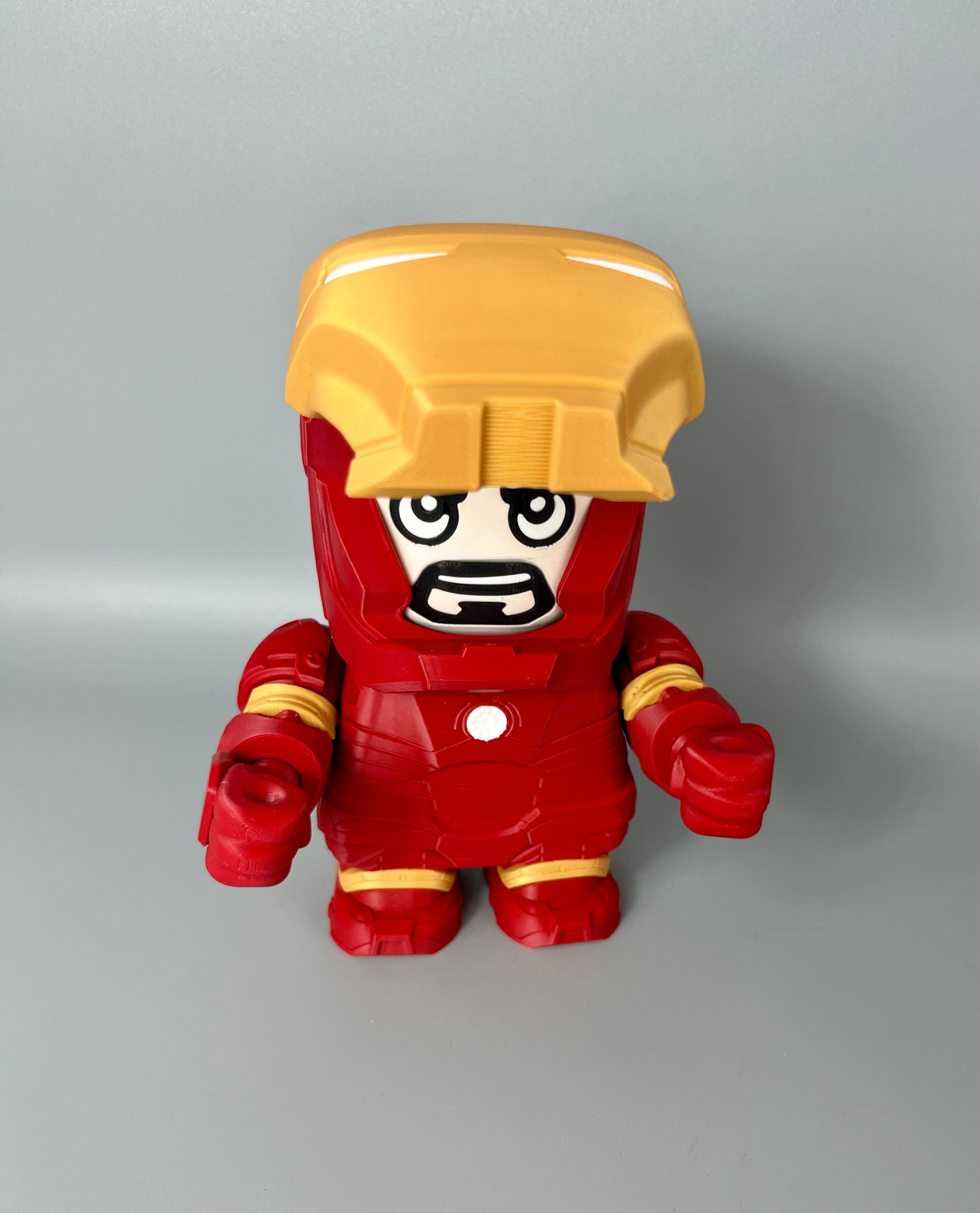 3D printed superhero with gold visor raised, exposed face with goatee and red and gold superhero suit, set on a grey background