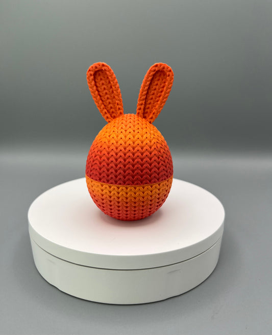 A 3D printed knitted bunny ear egg, displayed on a round white surface.