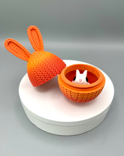 A 3D printed knitted bunny ear egg, opened up to show a little bunny inside. Displayed on a round white surface.