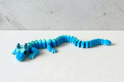 Colourful 3D printed articulated dragon with horns, white marble. The dragon has a flexible, segmented body and moveable little legs.