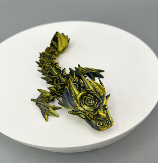 A small 3D-printed dragon with a prominent rose design on its head and small roses trailing along its body. Sat on a white circular base.