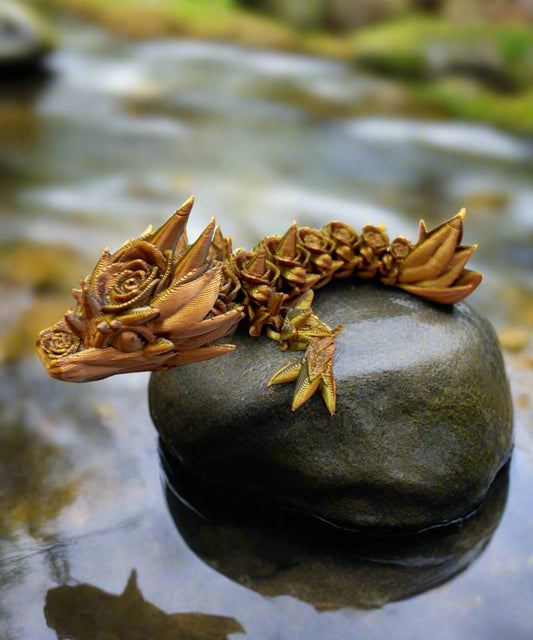 A small 3D-printed dragon with a prominent rose design on its head and small roses trailing along its body. Sat on a white circular base.