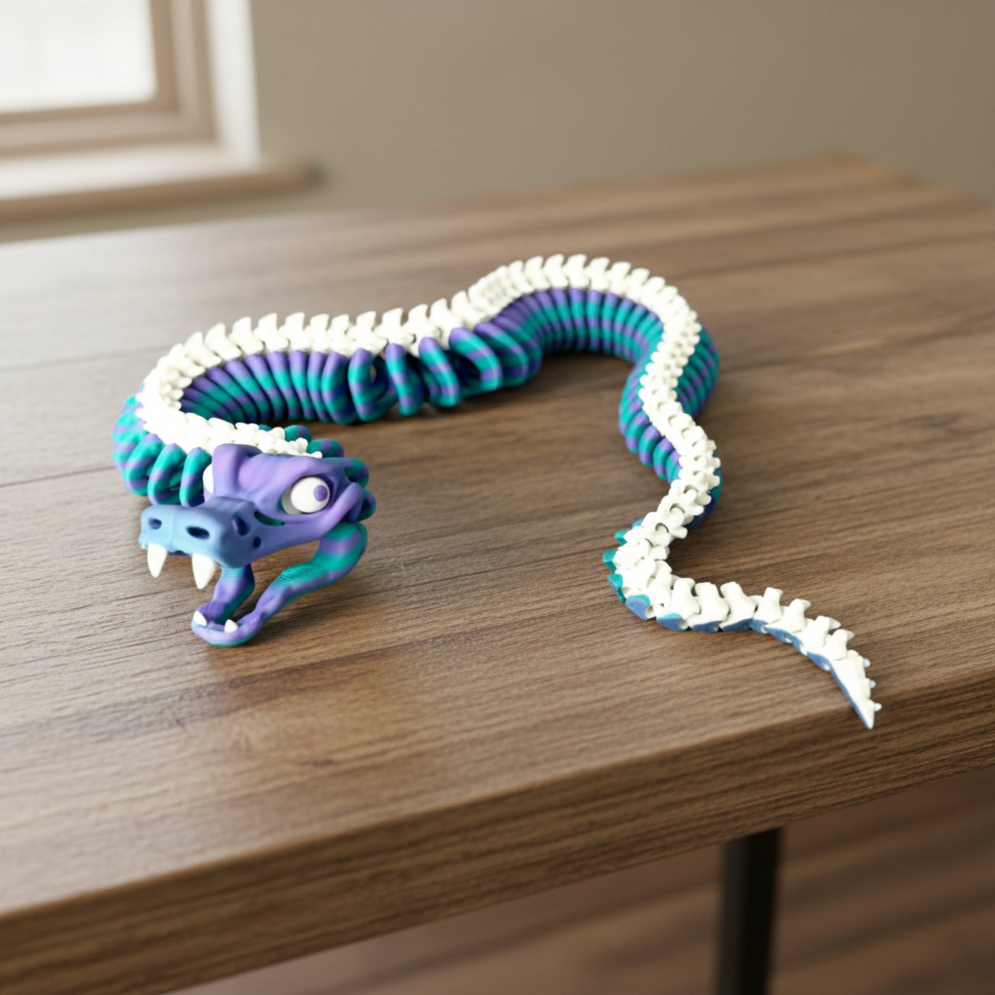 A 3D printed skeleton snake with flexible movement, featuring a moveable jaw, protruding teeth and cartoon-esque eyes. Laying on a wooden table. 